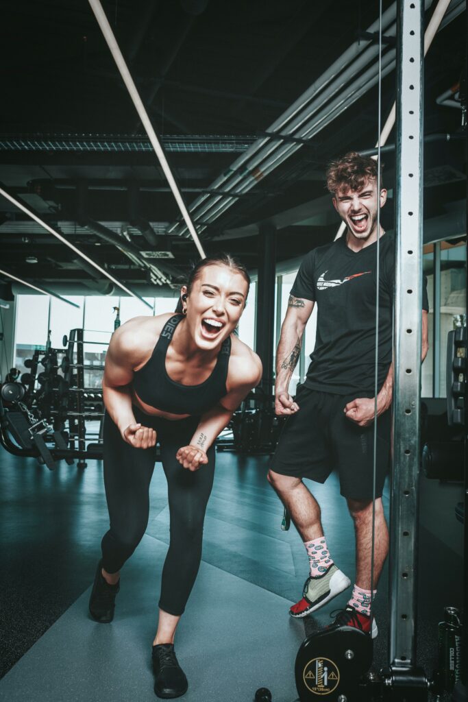 pexels-photo-10402987-10402987-1 Two friends laughing and flexing muscles during a gym workout, embodying a healthy lifestyle.