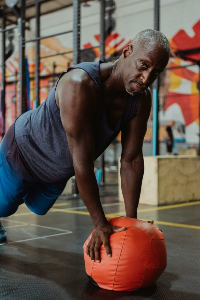 pexels-photo-4720544-4720544 Senior adult performing push-up exercise with a gym ball in a vibrant indoor gym setting.