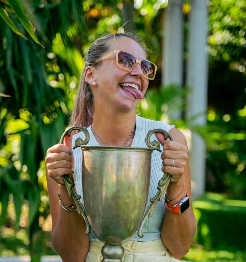 pexels-photo-6370111-6370111 A joyful woman proudly holding a trophy in a lush outdoor setting.